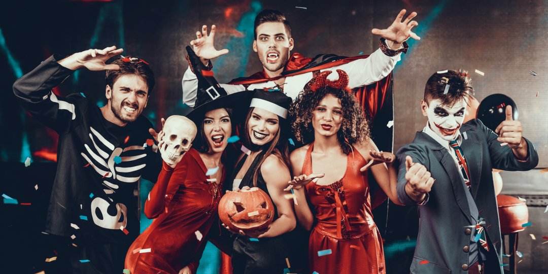 Grupa młodych szczęśliwych przyjaciół ubranych w kostiumy na Halloween bawi się razem i pozuje do zdjęć grupowych w klubie nocnym