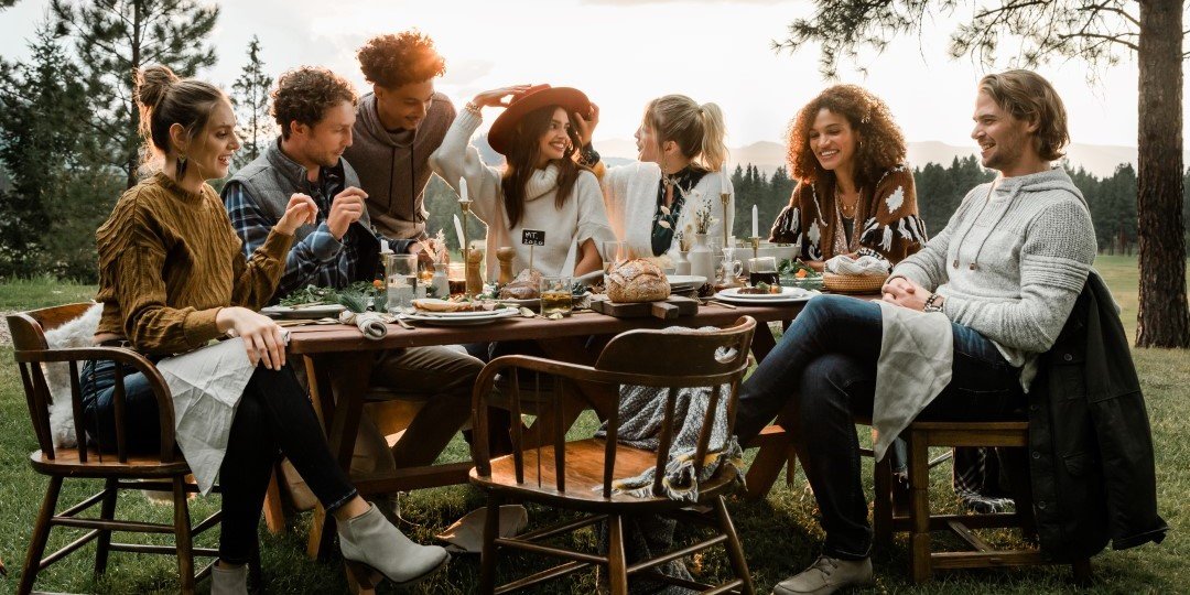Grupa młodych mężczyzn i kobiet spożywających posiłek przy stole na świeżym powietrzu, noszących klamry odzież jesienno-zimową