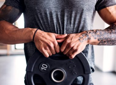 Portret atrakcyjnego sportowca z ciężką płytą z hantlami w klubie fitness