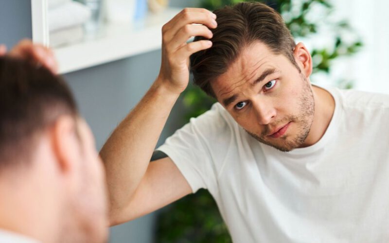 Zaniepokojony mężczyzna patrząc na swoje włosy w lustrze