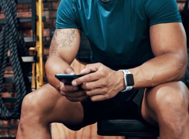 Przycięte zdjęcie sportowego młodego mężczyzny używającego smartfona w sali gimnastycznej