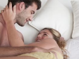 Mężczyzna i kobieta leżący w łóżku, trzymający się i uśmiechający.