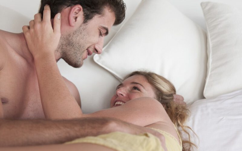 Mężczyzna i kobieta leżący w łóżku, trzymający się i uśmiechający.