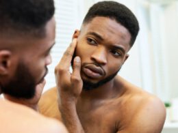 Młody Afroamerykanin facet sprawdzanie jego twarz skóra w lustro