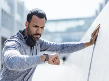 człowiek w ubrania treningowe biorąc przerwę od ćwiczeń, aby spojrzeć w dół na smartwatch