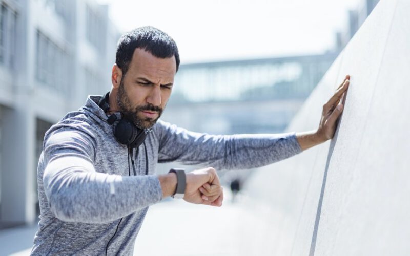 człowiek w ubrania treningowe biorąc przerwę od ćwiczeń, aby spojrzeć w dół na smartwatch