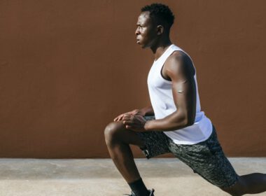 Athletic czarny człowiek robi lonży rozciąganie ćwiczenia na zewnątrz na tle ściany brązowy