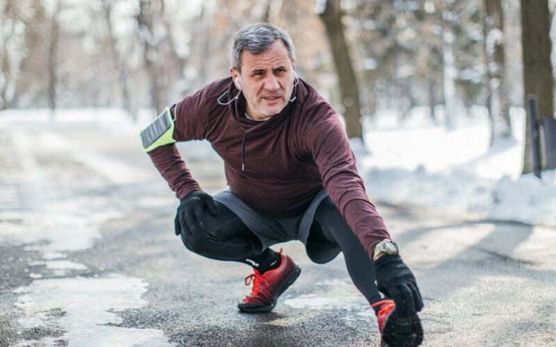 Starszy mężczyzna przygotowuje się do joggingu na świeżym powietrzu w parku, w mroźny zimowy dzień.