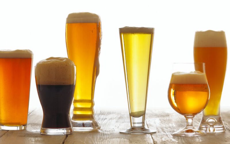 Asortyment piw piankowych serwowanych w sześciu przezroczystych szklankach o różnych kształtach i rozmiarach na drewnianej powierzchni.