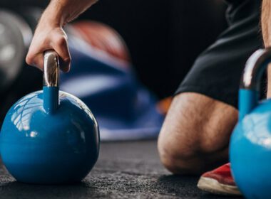 Mężczyzna klęczący w siłowni z kettlebells, przygotowując się psychicznie do podnoszenia ciężarów