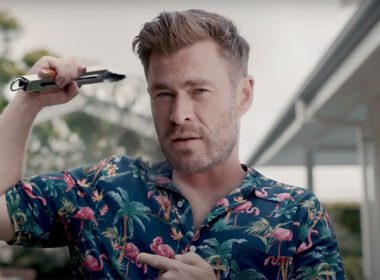 Chris Hemsworth w tropikalnej koszuli wskazujący na biceps w kampanii Centr dodaj