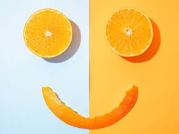 Pomarańczowe kawałki ułożone w kształt uśmiechu na pomarańczowym i niebieskim tle
