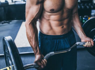 Bez koszulki muskularny mężczyzna trzyma sztangę robi ramię trening na siłowni