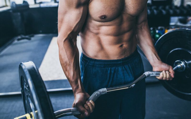 Bez koszulki muskularny mężczyzna trzyma sztangę robi ramię trening na siłowni