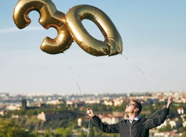 Mężczyzna trzymający balony helowe w kształcie numer 30 przeciwko miastu.