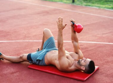 Muskularny mężczyzna bez koszulki leży na macie na korcie i rano wykonuje ćwiczenia z kettlebell
