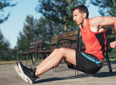 Mężczyzna wykonujący pośredni triceps z odpowiednią formą na ławce w parku, na zewnątrz.